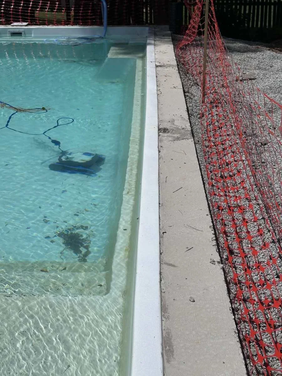 Pool under construction with water, exposed pool edge, and temporary orange safety fencing